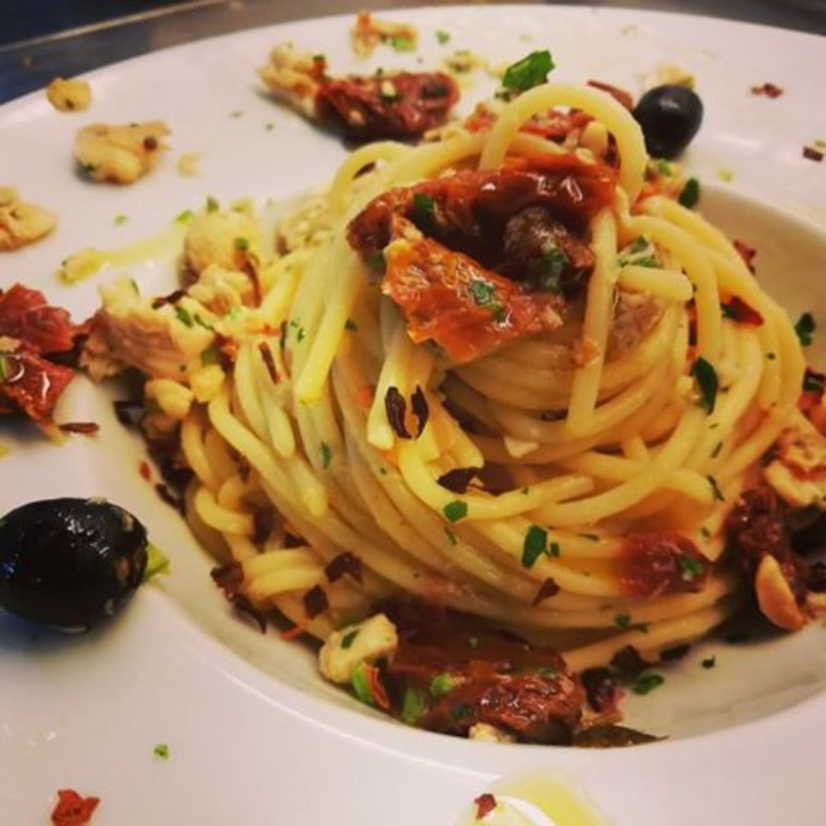 Piatto di spaghetti con pomodorini secchi e olive servito in osteria